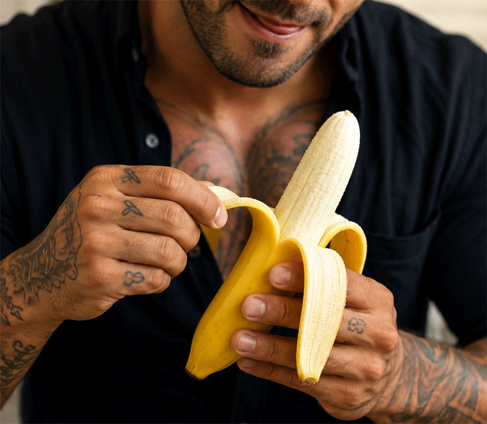 Mann mit tätowierten Händen schält eine Banane